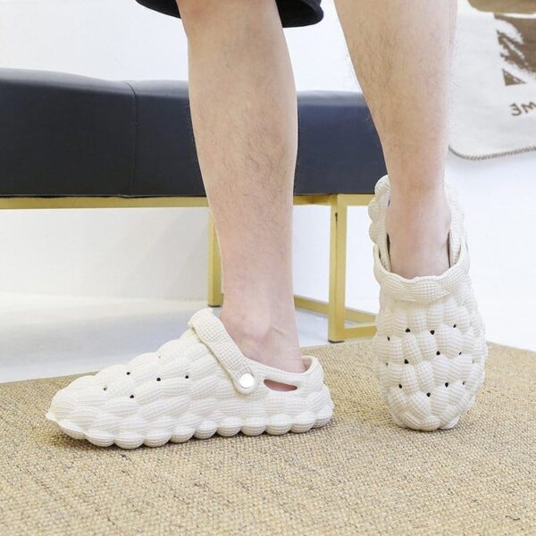 Person standing in white, chunky, textured Bubble Slippers on a beige floor mat.