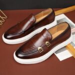 A pair of brown Men's Casual Leather Shoes with buckles on a dark background.