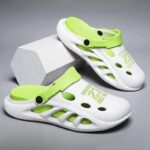 A pair of white and lime green ventilated clogs with adjustable straps, showcased as men's fashion casual non-slip sports slippers, displayed alongside a geometric white block.