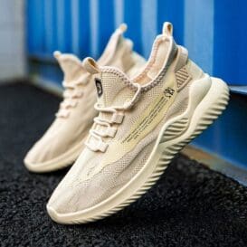 A pair of beige men’s lightweight breathable sneakers with a chunky sole and woven upper design, displayed outdoors against a blue background.