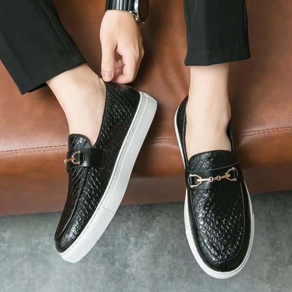 A pair of black Double Pin Buckle Loafers worn by someone with ankle-length trousers against a brown background.