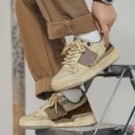 Person in brown trousers and stylish beige Skateboard Shoes stepping on a metal ledge.