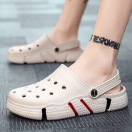 Person wearing trendy white men’s Summer Sandals with red stripe details on a textured pavement.