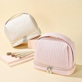 The makeup bag is displayed against a soft beige background. It appears to be made of a durable, waterproof polyurethane material with an elegant ribbed texture. The bag has a half-circle shape design with a flat base, allowing it to stand upright. The color of the makeup bag is a gentle pastel pink, complementing its sophisticated and clean aesthetic.