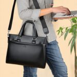 A person standing and using a laptop with a Men’s Business Simplicity Shoulder Messenger Bag slung over one shoulder. The bag is black, sleek, and appears to be made of leather, embodying a professional and minimalist aesthetic.