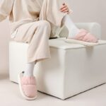 A woman relaxes on a white chair, donning pink slippers that provide warmth and a non-slip grip for outdoor use.