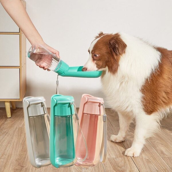 A person fills a green Portable Dog Water Bottle 550ml with water for a brown and white dog, with two other bottles in clear and pink colors displayed on the floor.