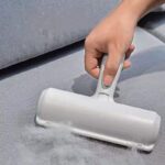 Hand using a pet hair remover lint roller on a grey fabric surface, effectively cleaning and removing lint and animal fur.