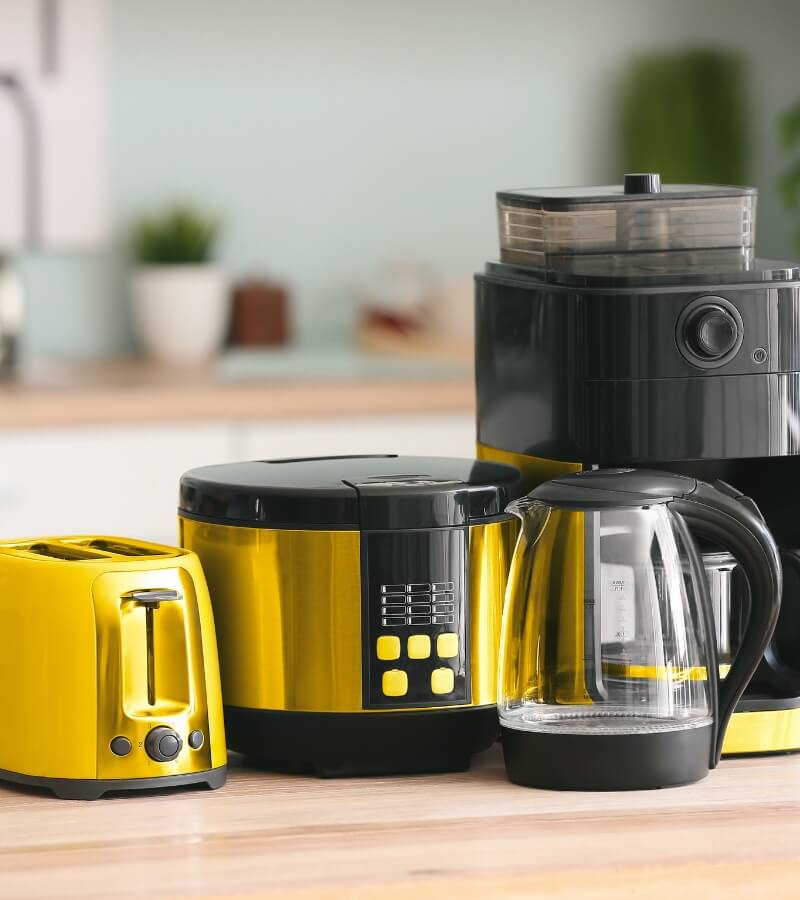 A modern kitchen countertop with a set of three black and yellow kitchen appliances. From left to right, there is a bright yellow toaster with a rounded top and a single dark knob on the front, a black coffee maker with a digital display and buttons.