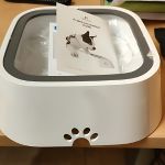 A modern, white cat litter box with a transparent, swing-top lid and a front entry hole shaped like a cat’s head.