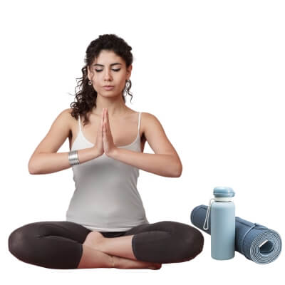 Woman in yoga suit practicing meditation pose with yoga accessories including a mat and water bottle.